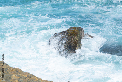 a large geologic formation of rock being pounded and splashed by strong current of sea water along a rocky coastal beach shore in the tropical region of the Pacific Ocean