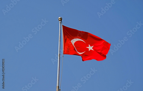 Turkish national flag on blue sky background. The flag on a flagpole flutters in the wind. The white star and crescent moon on red background.