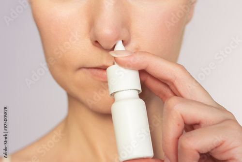 Close-up face of a young woman suffers from nasal congestion and runny nose. Woman uses nasal spray in her nose for nasal congestion. Rhinitis, cold, chronic diseases, allergy