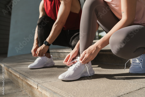 Close up hand of active young man and woman tying shoelace on her running shoes. Preparation before jogging exercise. Fitness and sport activity. Healthy exercise concept.