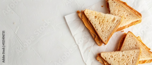 Triangular peanut butter sandwiches are arranged on wax paper, evoking simplicity and nostalgia with their classic comfort food appeal.