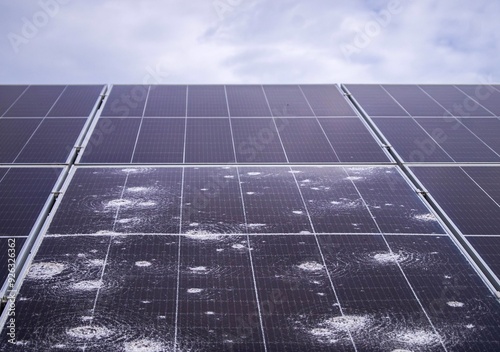 Hail-damaged solar panel close-up with cracked photovoltaic cells under overcast skies, showcasing the effects of extreme weather on renewable energy technology.