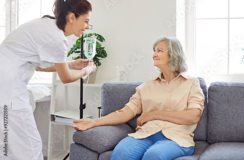 Senior woman with intravenous drip sitting on couch, physician, nurse doctor fixing IV drip infusion, geriatrics hospital eldercare, therapy to infuse vitamins, chemotherapy to maintain health clinic