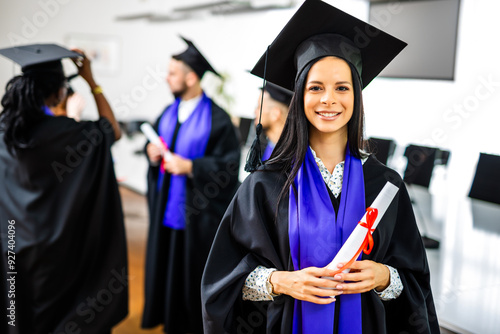 Portrait of graduate student in toga holding her diploma in front of her friends.