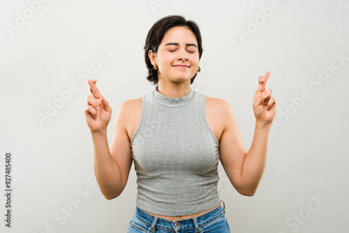 Cute woman smiles with her eyes closed, crossing her fingers for good luck, exuding optimism and faith in a hopeful expression