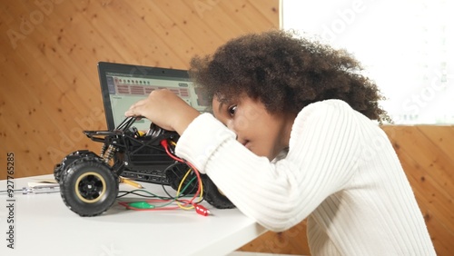 Smart african girl build robotic car while using wires while using laptop setting or writing prompt code. Skilled female student working on computer in STEM technology online classroom. Erudition.