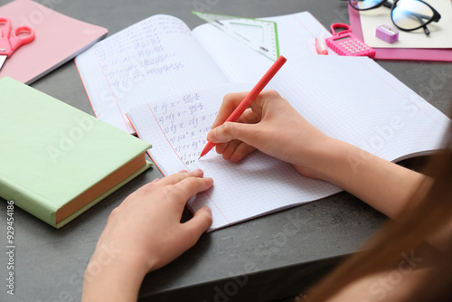 Woman writing math formulas in copybook at dark table