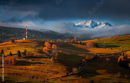 Osturna, Slovakia - Panoramic view on High Tatras mountains National Park on a sunny autumn morning with warm golden sunrise colors on foliage, radio tower and foggy mountains at background