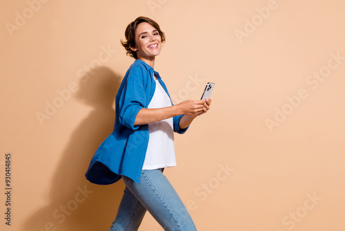 Photo of cheerful young hr manager lady in smart casual outfit use smartphone when strolling at office isolated on beige color background