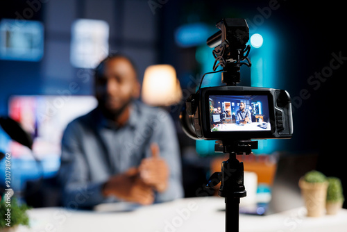 Professional camera capturing footage of streamer chatting with online audience. Trending content creator in blurry background discussing with fans filming with high quality recording tech