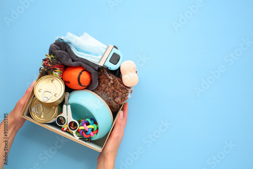 Donation box with pet supplies and food in female hand over blue background. Pet care, charity, animal shelter support concept.