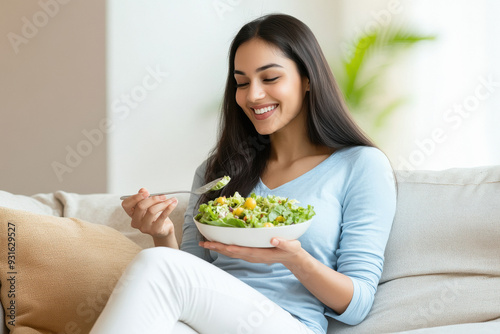 attractive indian woman standing and eating salad at the kitchen counter