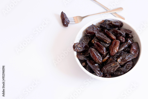 Dates inside a bowl on a white background with a dessert fork