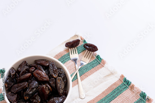 Bowl with portion of dried dates and forks with dates on top of a striped cloth