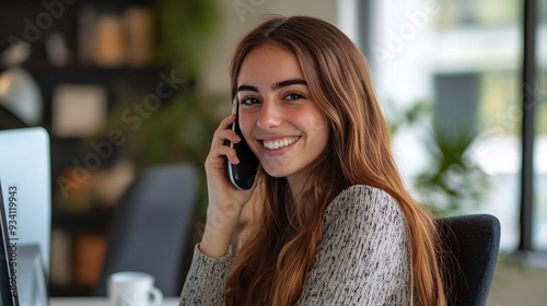 brown haired girl talking on the phone, working on a computer, sitting and smiling, in a modern office