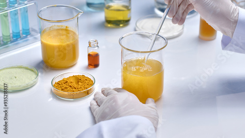 In the middle of white lab table displaying a glass beaker, which contains turmeric extract and being stirred by a glass rod in scientist hand. Photo of lab theme from high angle view, space for text