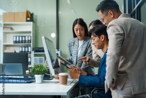 In an office, an Asian team meets at a desk, analyzing financial data on a monitor. They discuss business finance, operational guidelines, and strategies for success, data-driven decision-making.