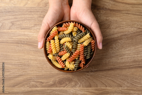 Raw fusilli pasta in bowl holding by hand on wooden background, Food ingredient, Table top view