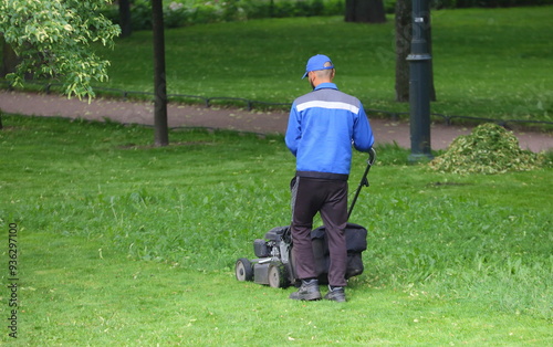 A worker in a blue uniform mows the grass with a lawn mower, Mikhailovsky Garden, St. Petersburg, Russia, June 14, 2024