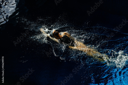 Female athlete swims with a back stroke. Splashes of water scatter in different directions