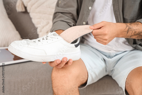 Young man with flat feet inserting orthopedic insole into sneaker at home, closeup