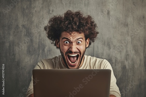 Excited man with curly hair using laptop