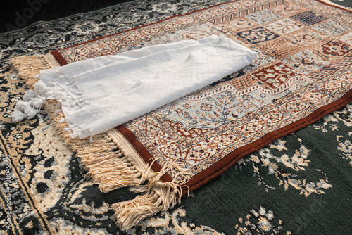 A white turban and a brown patterned prayer mat on a green carpet. The prayer mat of the imam of the congregational prayer. Muslim prayer.