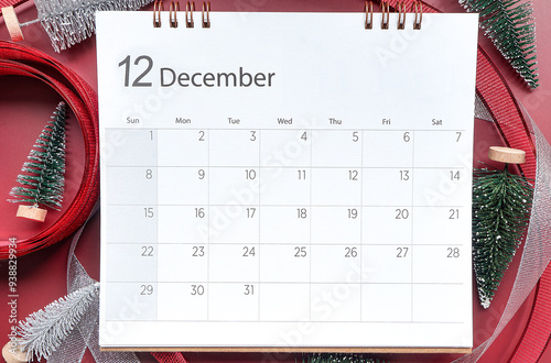 December 2024 calendar schedule , Top view shot featuring calendar with December month, little Christmas tree, glitter silver ribbon and red ribbon on red background. Chrismas and New year concept.