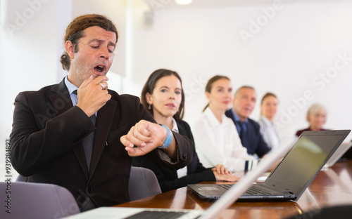 Bored mature white male office employee sitting at tiring slow team meeting, having urge to yawn, impatiently waiting for the end of the meeting