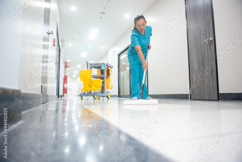 A mop operator in a blue uniform cleans new epoxy floor protection suits in an empty hospital warehouse.