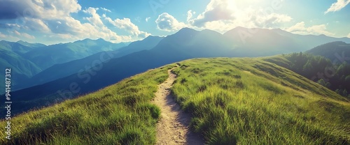 Winding path through green mountain meadows with a view of distant peaks and a bright, sunny sky.