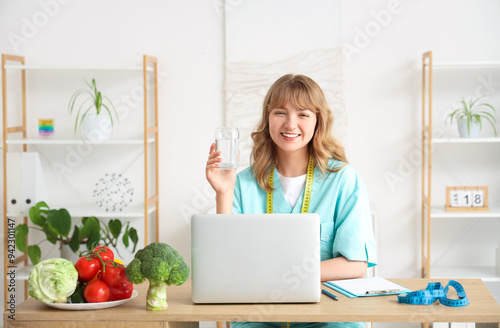 Female nutritionist with glass of water at table in kitchen