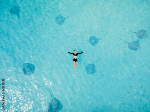 Woman swims in sea with stingrays in Maldives. Stingray fishes and floating woman in blue ocean. Drone view