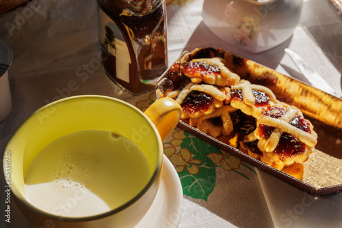 colazione con una tazza di latte, del caffè solubile e dei dolci a base di pasta frolla e marmellata