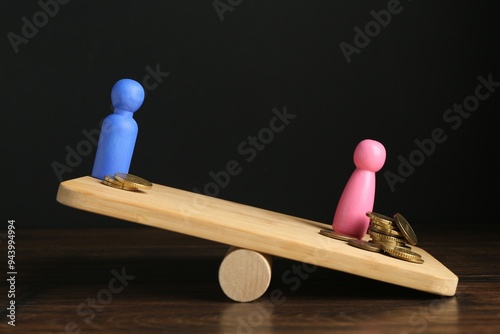 Financial inequality. Male and female figures with different amount of coins showing imbalance on scales on wooden table