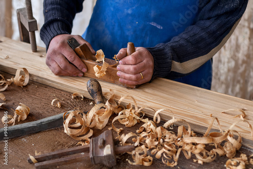 craftsman hand finishes a wooden board clamped with a vice using an old blade and a plane