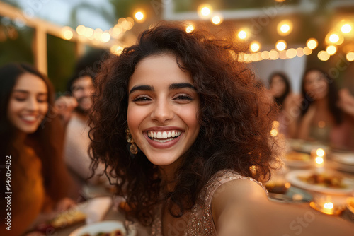 happy Indian friends taking a selfie at a dining table with food on it. People are sitting around the round dinner table and laughing.