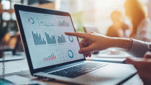 Hand pointing closely at detailed data and analytical graphs displayed on a laptop screen during a business meeting, emphasizing critical information analysis.