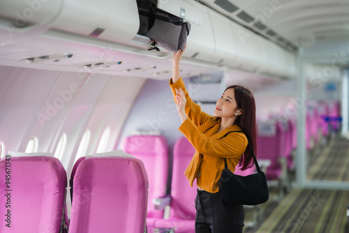 Ready for Takeoff: A young woman stows her carry-on luggage in the overhead compartment, eager for her flight to begin. 