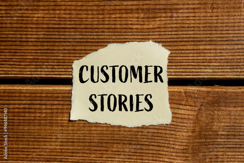 Customer stories message written on ripped torn paper piece with wooden background. Conceptual customer stories symbol. Copy space.