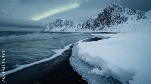 An image of a frosty shoreline extends to the snow-covered mountains in the distance, creating a tranquil environment under the moody sky, with waves gently lapping the shore.