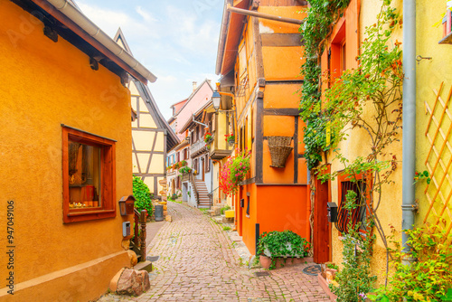 Colorful half-timbered buildings in a narrow cobblestone alley in the historic old town district of the touristic village of Eguisheim, France, in the Alsace region.