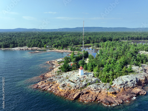 Old lighthouse on a rocky outcrop on Lake Huron's northern shore with forest and mountains in the background