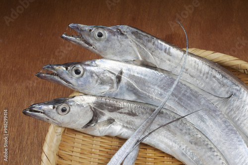 Close-up of head of three raw silver cutlass fish with sharp teeth on a bamboo basket, South Korea