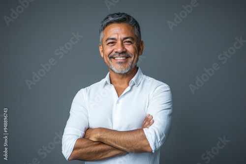 Smiling confident latin hispanic mature business man standing crossed arms on grey background.