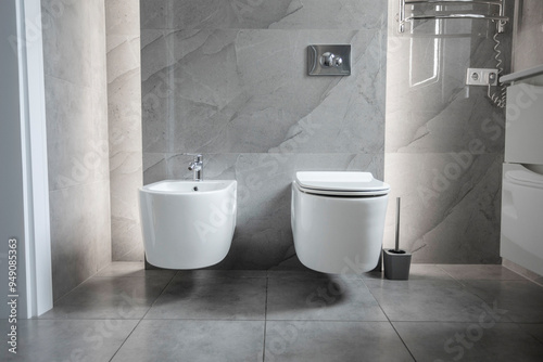 White wall-hung bidet and toilet, on gray ceramic tiles in minimalist and modern bathroom interior