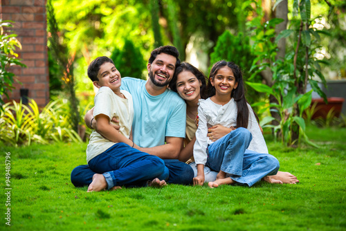 Happy Indian family of four sitting in park, embracing and smiling at camera, enjoying quality time