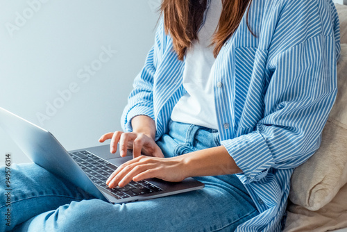 Close-up of a young woman comfortably seated on a hotel bed using a laptop with wireless wifi connection. Represents the modern lifestyle of professionals working remotely while traveling for business