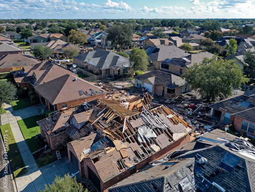 A house with a lot of damage is shown from the air. The house is surrounded by other houses, and the damage is extensive