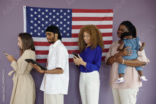 People using their gadgets while standing in queue in voting centre with American flag on the wall